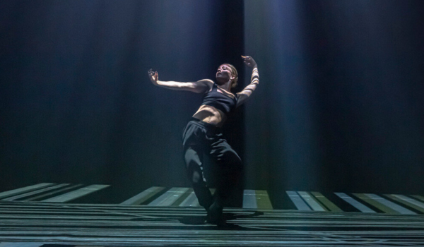 Lewis Major dancing on stage in a black crop and black pants with his arms in the air