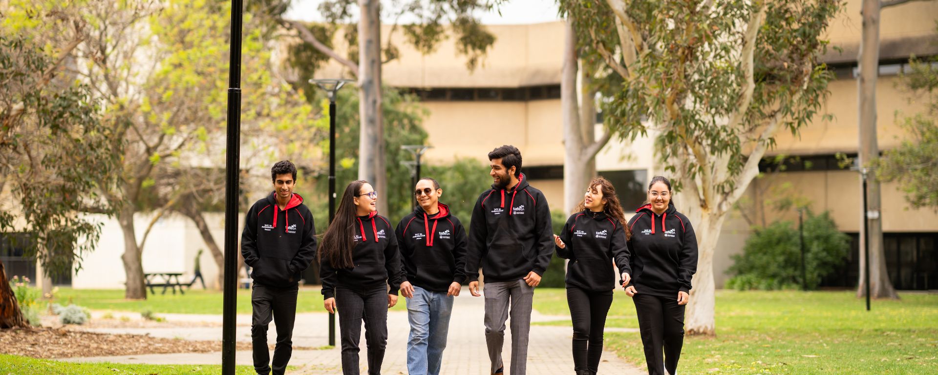 Six TAFE SA student mentors in branded hoodies walking together across a green campus