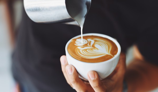 Person pouring milk into a coffee cup