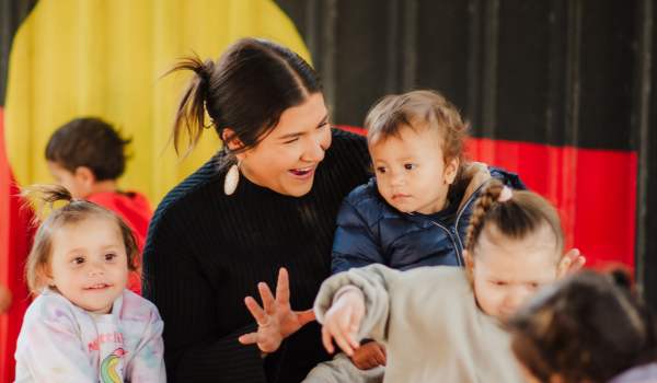 Childhood educator playing with children in front of an Aboriginal flag