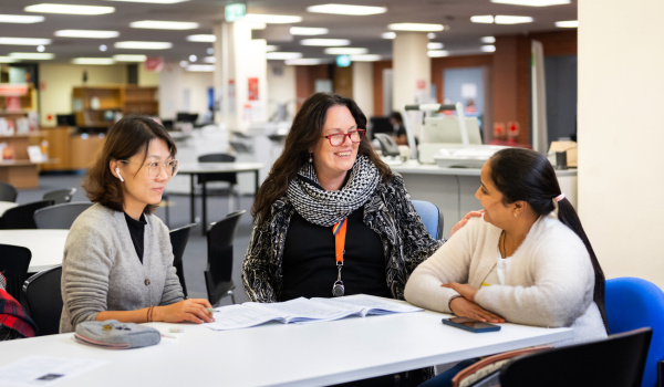 Teacher sitting with two students either side of her, smiling with paper on desk